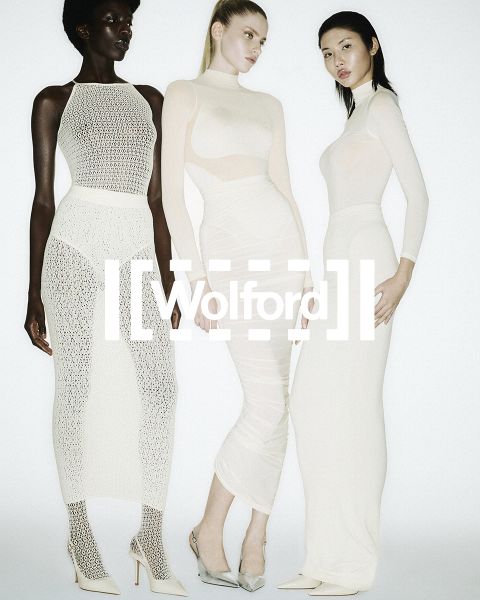 Drei Frauen in durchsichtigen, weißen, figurbetonten Kleidern und hochhackigen Schuhen posieren gemeinsam vor einem weißen Hintergrund mit dem fett gedruckten Schriftzug "Wolford".