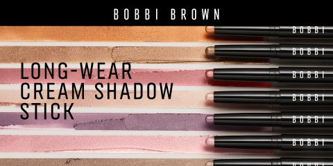 Eine Auswahl langanhaltender Creme-Lidschattenstifte von Bobbi Brown in verschiedenen Farbtönen, horizontal auf einer strukturierten Oberfläche präsentiert. Jeder Stift ist geöffnet und gibt die cremigen Farben frei. Der Markenname ist auf den Kappen sichtbar.
