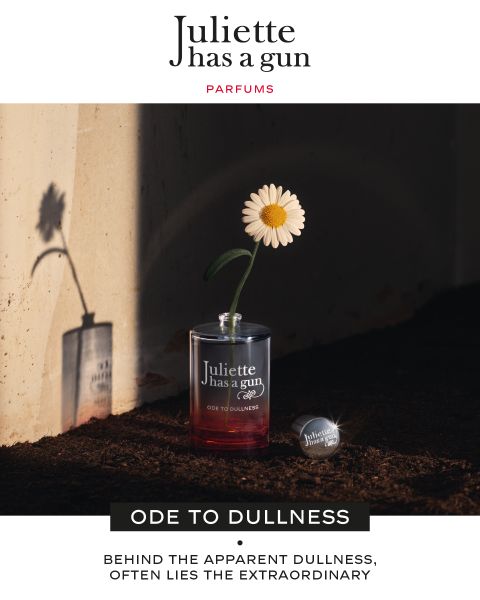 Auf einem Sims steht ein durchsichtiges Parfümfläschchen aus Glas mit den Aufschriften „Juliette has a gun“ und „ODE TO DULLNESS“. In dem Fläschchen befindet sich eine einzelne weiße Gänseblume. Der Schatten der Gänseblume wird auf eine dahinterliegende Wand geworfen. Sonnenlicht erzeugt einen dramatischen Effekt.