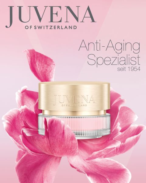 Vor einer großen rosa Blume steht ein Behälter mit Anti-Aging-Creme von Juvena of Switzerland. Der Hintergrund ist ein Farbverlauf aus Rosa und Weiß. Der Text lautet: „Juvena of Switzerland, Anti-Aging-Spezialist seit 1954.“.
