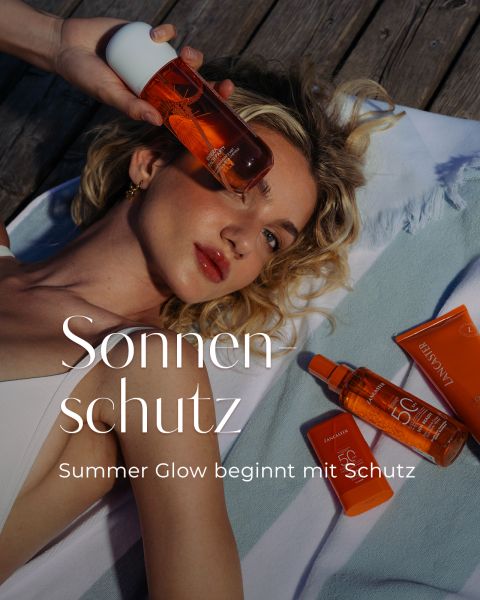 Eine Frau liegt auf einem Handtuch und hält eine Flasche Sonnencreme in der Hand; daneben liegen weitere Sonnencremeprodukte. Text: „Sonnenschutz. Sommerglow beginnt mit Schutz.“.