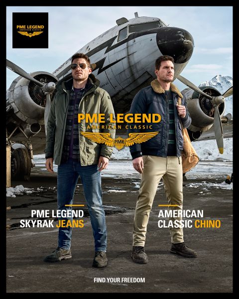 Zwei Männer stehen vor einem historischen Flugzeug mit schneebedeckten Bergen im Hintergrund. Einer trägt PME Legend Skyrak Jeans und eine grüne Jacke, der andere trägt American Classic Chinos und eine marineblaue Jacke. Der Text auf dem Bild macht Werbung für PME Legend-Kleidung.