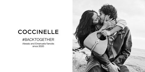 Ein Schwarzweißfoto zeigt ein Paar, das sich an einem felsigen Strand lächelt und umarmt. Der Mann hält eine Handtasche. Der Text links lautet: „Coccinelle #BACKTOGETHER Alessio und Emanuela sind seit 2020 verlobt.“.