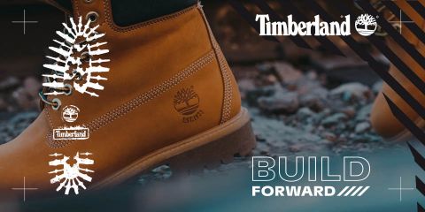 Nahaufnahme eines Timberland-Stiefels auf felsigem Boden, mit dem Timberland-Logo und dem Satz „BUILD FORWARD“ auf der rechten Seite. Der Stiefel ist hellbraun und hat eine robuste Sohle, die einen Outdoor- und Abenteuer-Look ausstrahlt.