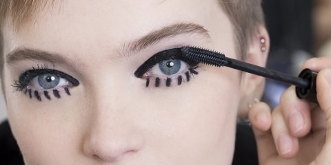 Nahaufnahme einer Person, die Mascara auf ihre oberen Wimpern aufträgt, wobei ein kräftiger Eyeliner für einen dramatischen Look sorgt. Der Fokus liegt auf dem Auge und der Mascara-Bürste, wodurch der Vorgang des Schminkens hervorgehoben wird.
