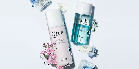 Zwei Dior-Hautpflegeflaschen sind von rosa und blauen Blumen umgeben. Eine Flasche ist hellrosa mit „Life“ auf dem Etikett, die andere ist blaugrün. Überall sind Wassertropfen verstreut, was für eine frische und elegante Präsentation sorgt.