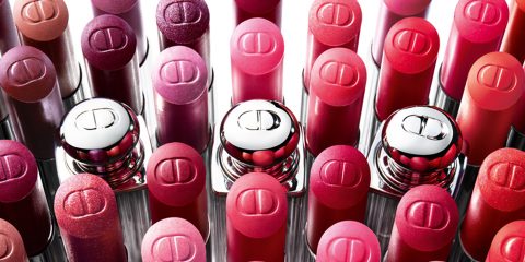 Verschiedene Lippenstifte in unterschiedlichen Rot- und Pinktönen sind in Reihen angeordnet. Jeder Lippenstift hat eine glänzende Kappe mit eingeprägtem Logo, wodurch ein farbenfrohes und optisch ansprechendes Muster entsteht.