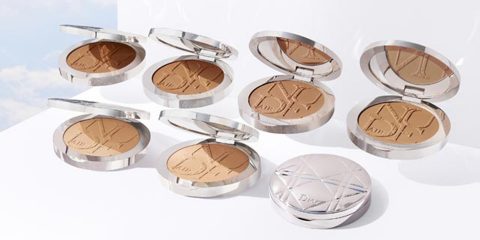 Eine Sammlung von sieben geöffneten Make-up-Kompakten, die verschiedene Farbtöne von Kompaktpuder mit komplizierten Designs zeigen. Eine Kompakte ist geschlossen und wird auf einer reflektierenden weißen Oberfläche vor dem Hintergrund eines bewölkten Himmels präsentiert.