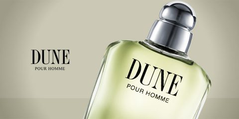 Vor einem hellen Hintergrund ist eine Flasche „Dune Pour Homme“ mit silbernem Verschluss zu sehen. Die Flasche ist teilweise geneigt und auf der linken Seite ist der Produktname in fetten Buchstaben zu sehen.