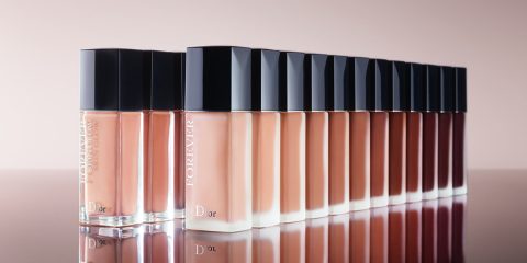 Eine Reihe von Dior Forever Foundation-Flaschen in verschiedenen Farbtönen, angeordnet von hell bis dunkel. Die eleganten Glasflaschen haben schwarze Kappen, die auf einer glänzenden Oberfläche reflektieren. Der Hintergrund hat einen weichen, neutralen Ton.