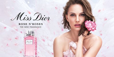 Eine Frau mit einer rosa Blume steht neben einer Flasche Miss Dior Rose N'Roses-Parfüm. Der Hintergrund ist ein fließender, zarter Stoff mit rosa Blütenblättern. Der Text auf dem Bild lautet „Miss Dior Rose N'Roses, der neue Duft.