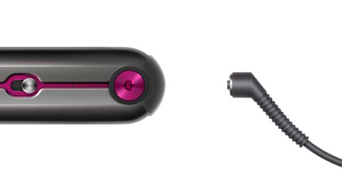 Nahaufnahme eines grau-rosa Haarstyling-Tools neben einem schwarzen, abgewinkelten Netzkabelstecker auf weißem Hintergrund.
