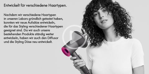 Eine Person mit lockigem Haar hält lächelnd einen Haartrockner. Der Text ist auf Deutsch und beschreibt die Entwicklung von Produkten für verschiedene Haartypen. Der Haartrockner verfügt über einen Diffusoraufsatz. Der Hintergrund ist grau.