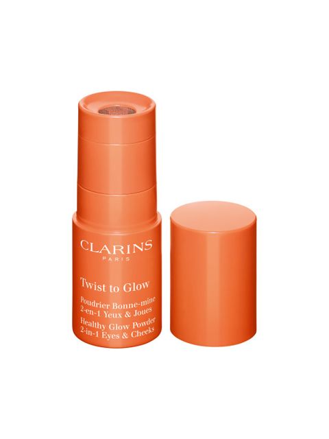 Ein orangefarbener zylindrischer Behälter mit Clarins Twist to Glow ohne Deckel, der einen Puderapplikator freigibt. Auf der Verpackung steht ein Text, der für die Verwendung für einen gesunden Glanz auf Augen und Wangen wirbt.