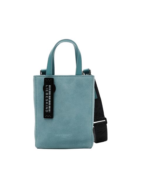 Türkisfarbene Wildlederhandtasche mit schwarzem verstellbarem Schultergurt und schwarzem Anhänger mit der Aufschrift „LIEBESKIND BERLIN“. Die Tasche hat kurze Henkel und eine Logoprägung unten vorne.
