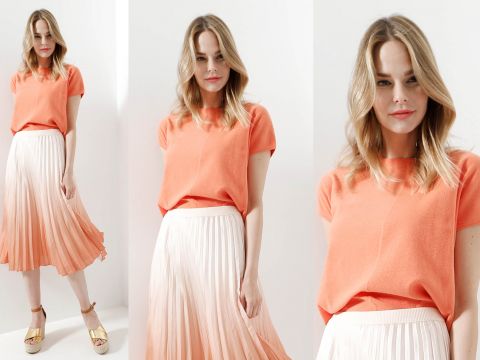 Eine Frau in einem orangefarbenen Oberteil und einem weißen Faltenrock posiert in drei Bildern. Sie hat schulterlanges blondes Haar und lächelt leicht. Den Look rundet sie mit Sandalen mit Knöchelriemen ab. Der Hintergrund ist in einer schlichten hellen Farbe gehalten.