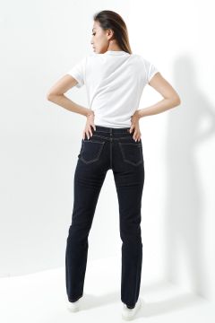 Eine Person steht vor einem weißen Hintergrund und blickt von der Kamera weg. Sie trägt ein weißes T-Shirt, dunkle Jeans und weiße Turnschuhe und hat die Hände in die Hüften gestemmt.