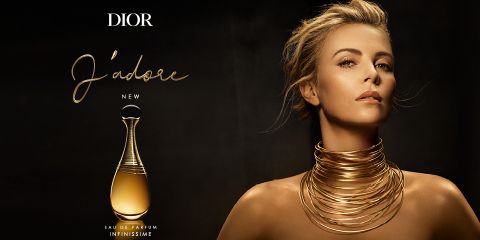 Eine Person mit raffinierter Frisur und mehreren goldenen Halsketten posiert elegant vor einem dunklen Hintergrund. Daneben steht eine elegante Flasche Dior „J'adore“ Eau de Parfum Infinissime mit einem gold-schwarzen Design.