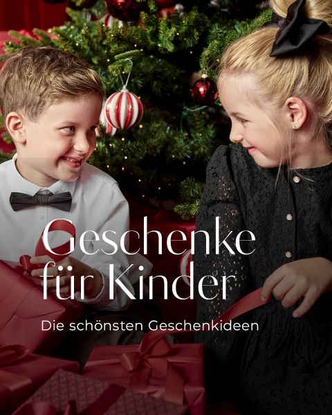 Zwei Kinder, ein Junge mit weißem Hemd und Fliege und ein Mädchen in einem schwarzen Kleid, sitzen vor einem geschmückten Weihnachtsbaum, lächeln sich an und halten Geschenke in der Hand. Der Text auf Deutsch lautet: "Geschenke für Kinder. Die schönsten Geschenkideen.