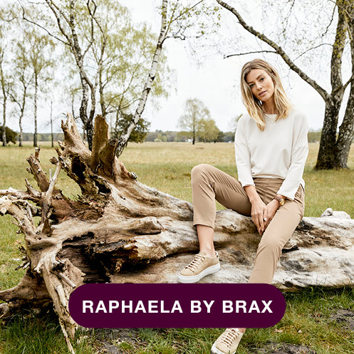 Eine Frau in legerer Kleidung sitzt auf einem großen umgestürzten Baum auf einer Wiese mit vereinzelten Bäumen. Unten ist der Text „RAPHAELA BY BRAX“ zu sehen.