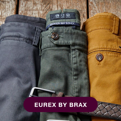 Drei hochgekrempelte Hosen in Dunkelblau, Olivgrün und Senfgelb liegen vertikal auf einer Holzfläche. Auf einem Etikett steht „Eurex by Brax“.