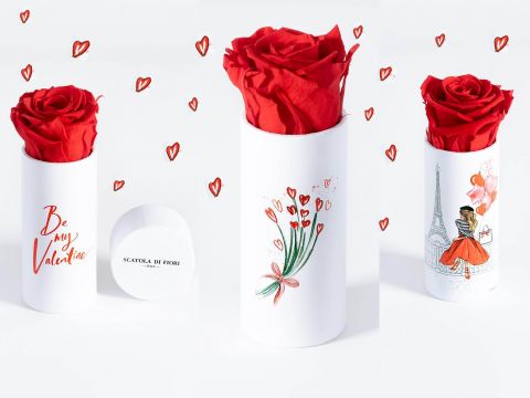 Drei weiße zylindrische Schachteln mit illustrierten Motiven, jede enthält eine einzelne rote Rose. Auf der ersten Schachtel steht „Sei mein Valentinsschatz“. Die zweite ist von gekritzelten Herzen umgeben. Die dritte zeigt die Skizze eines Paares in der Nähe des Eiffelturms.