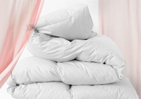 Ein Stapel weißer Kissen vor weißem Hintergrund, teilweise eingerahmt von durchsichtigen rosa Vorhängen an den Seiten. Die Kissen wirken plüschig und flauschig, lässig angeordnet.