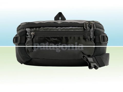 Eine schwarze Gürteltasche von Patagonia mit mehreren Reißverschlüssen und verstellbaren Riemen ist vor einem geteilten Hintergrund in Hellblau und Grün zu sehen.