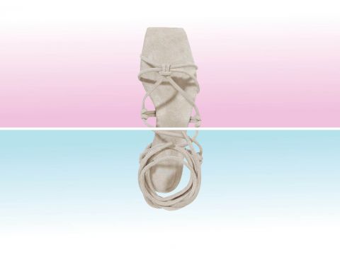 Eine beige Sandale mit quadratischer Spitze und aufwendigen Wickelriemen ist vor einem Hintergrund zu sehen, der in rosa und blaue Farbverlaufshälften geteilt ist. Die Sandale ist aus einer Draufsicht zu sehen.