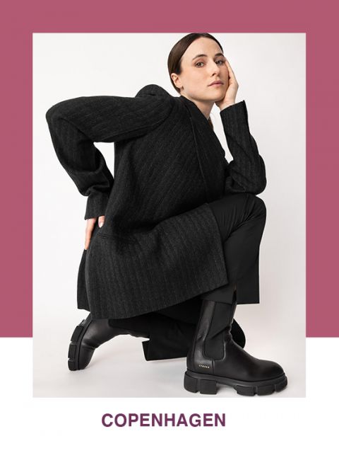 Eine Person posiert in einem schicken schwarzen Outfit, darunter Mantel und klobige Stiefel, vor einem weißen Hintergrund mit violettem Rahmen. Unten ist in violetter Schrift das Wort „Kopenhagen“ zu sehen.