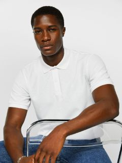 Mann sitzt auf einem durchsichtigen Stuhl, trägt ein weißes Poloshirt und Bluejeans vor einem schlichten weißen Hintergrund.