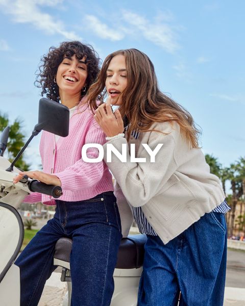 Zwei Frauen sitzen lachend auf einem weißen Roller im Freien. Die eine trägt einen rosa Pullover und Jeans, die andere einen weißen Pullover und Jeans. Das Wort „ONLY“ ist über das Bild gelegt. Im Hintergrund sind ein klarer Himmel und Palmen zu sehen.