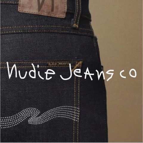 Nahaufnahme der Gesäßtasche einer dunkelblauen Jeans mit orangefarbenen Nähten und einem Wellendesign aus kleinen Nieten. Am Hosenbund ist ein brauner Lederpatch zu sehen. Über dem Bild steht in Weiß der Markenname „Nudie Jeans Co“.