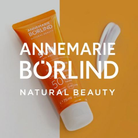 Vor einem hellen Hintergrund steht eine orangefarbene Tube Annemarie Börlind Natural Beauty Anti-Aging Sonnencreme mit LSF 50. Neben der Tube ist ein weißer Streifen der Creme zu sehen.