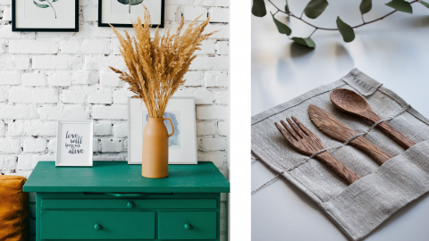 Eine grüne Kommode mit einer Vase mit Trockenblumen und gerahmten Kunstwerken steht vor einer weißen Backsteinwand. Rechts daneben liegt ordentlich ein Satz Holzutensilien auf einer Stoffmatte neben Eukalyptusblättern.