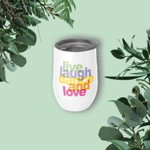 Ein weißer Becher mit dem bunten Text „Live Laugh Dance and Love“ steht auf einem hellgrünen Hintergrund. Um den Becher herum sind an den Ecken grüne Zweige mit Blättern angebracht, die eine natürliche, erfrischende Atmosphäre schaffen.