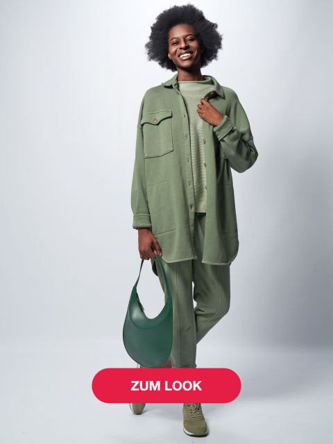 Lächelnde Person, gekleidet in ein stylisches Salbeigrün-Outfit mit langem Hemd, Hose und Turnschuhen, hält eine passende grüne Tasche. Der Hintergrund ist schlicht hellgrau und unten befindet sich ein roter Button mit dem Text „ZUM LOOK“.