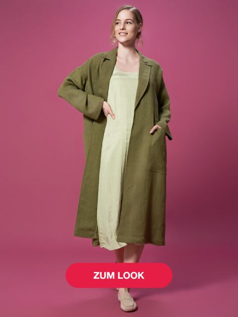 Eine Person, die einen langen grünen Mantel über einem hellgrünen Kleid trägt, posiert mit den Händen in den Taschen. Der Hintergrund ist rosa und unten befindet sich ein roter Button mit dem Text „ZUM LOOK“.