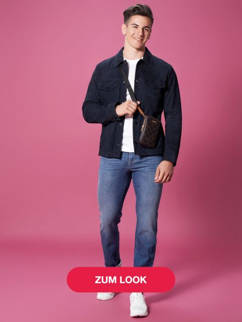 Eine Person steht lächelnd vor einem rosa Hintergrund und trägt eine dunkle Jacke, ein weißes T-Shirt, blaue Jeans und weiße Turnschuhe. Sie trägt eine kleine Umhängetasche. Auf dem Bild ist ein roter Button mit der Aufschrift „Zum Look“.