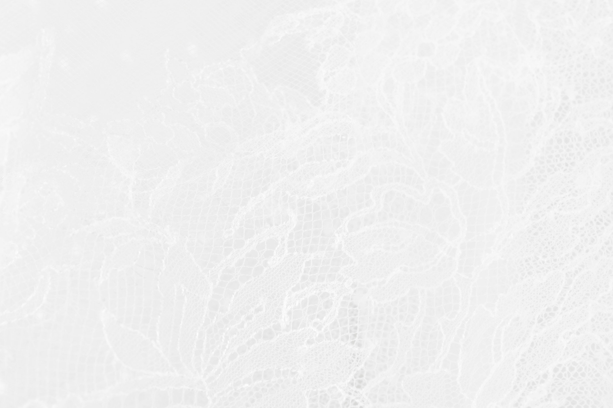Nahaufnahme eines zarten weißen Spitzenstoffs mit einem komplizierten Blumenmuster. Die Textur zeigt ein feines Netz mit detaillierten Blumen- und Blattmustern und vermittelt ein Gefühl von Eleganz und Subtilität.