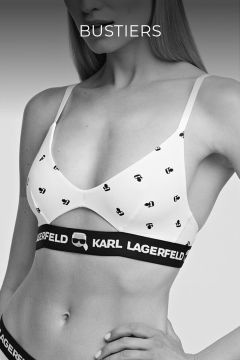 Eine Frau trägt ein weißes Bustier mit kleinen schwarzen Symbolen und elastischen Trägern mit der Marke „Karl Lagerfeld“. Das Bild ist schwarzweiß und sie ist teilweise von den Schultern bis zu den Hüften sichtbar. Oben steht das Wort „BUSTIERS“.
