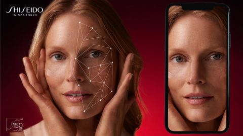 Eine Frau hält ihre Hände vors Gesicht. Auf der linken Seite hebt ein geometrisches Muster ihre Gesichtszüge hervor. Auf dem Smartphone-Bildschirm rechts von ihr ist eine vergrößerte Ansicht ihres Gesichts zu sehen. Der Hintergrund ist rot, in der Ecke steht „Shiseido“.