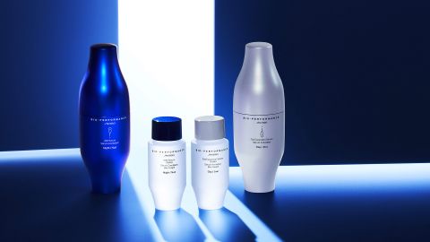 Vier Hautpflegeflaschen in modernem Design werden auf einer reflektierenden Oberfläche präsentiert. Die Flaschen variieren in Größe und Farbe: zwei sind weiß, eine silberfarben und eine blau. Ein Scheinwerfer von oben wirft ein Licht und sorgt so für eine elegante und stilvolle Ästhetik.