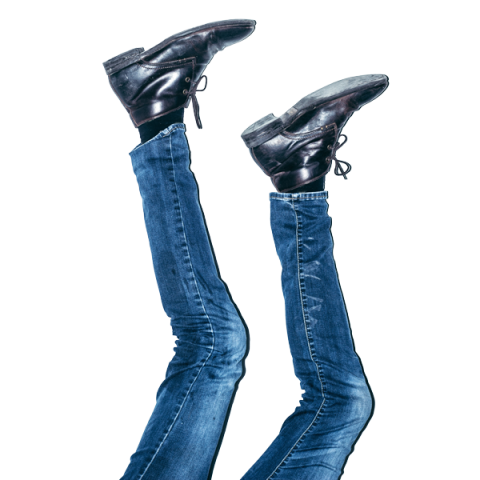 Ein Paar Beine in Bluejeans und schwarzen Schuhen ragen vor einem weißen Hintergrund in die Luft und erzeugen so die Illusion, als stünden sie auf dem Kopf.
