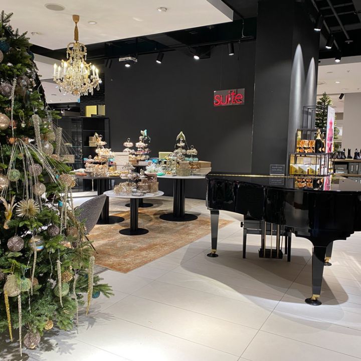 Ein luxuriöses Ladeninterieur mit einem geschmückten Weihnachtsbaum, einem schwarzen Flügel und einer Auslage mit kunstvollen Kuchen und Gebäck auf eleganten Ständen. Das Ambiente ist festlich und edel, mit einem Kronleuchter und stilvollem Dekor.