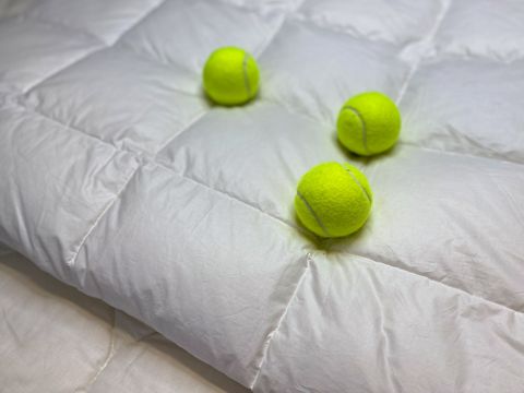 Drei neongrüne Tennisbälle liegen auf einer flauschigen, weißen Steppdecke und bilden einen weichen und gemütlichen Kontrast.