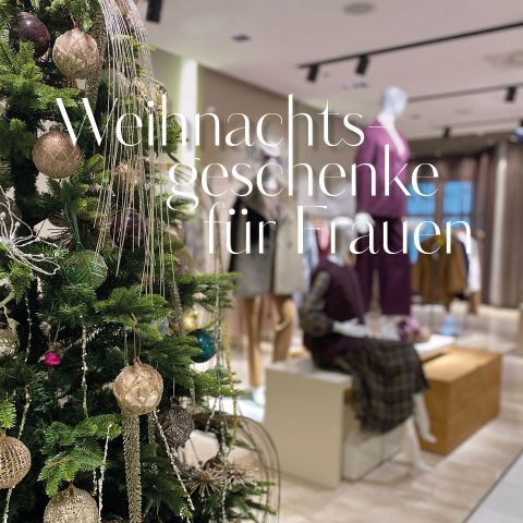 In einem Modegeschäft steht ein geschmückter Weihnachtsbaum mit Ornamenten. Im Hintergrund sind stylische Schaufensterpuppen in Damenkleidung zu sehen. Der Textüberzug lautet „Weihnachtsgeschenke für Frauen“.