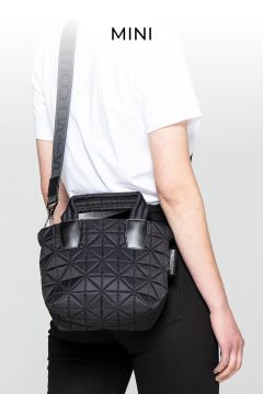 Eine Person in weißem T-Shirt und schwarzer Hose trägt eine kleine schwarze Stepptasche mit Ledergriffen und Schultergurt. Darüber ist das Wort „MINI“ zu sehen. Der Hintergrund ist hellgrau.