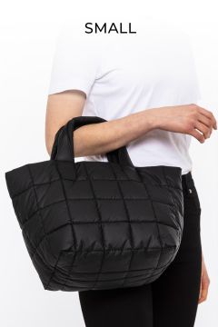 Person hält eine kleine, schwarze, gesteppte Handtasche. Sie trägt ein weißes Hemd und eine schwarze Hose. Über der Tasche steht das Wort „SMALL“.
