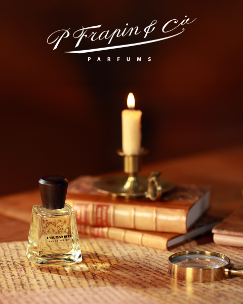 Auf alten Büchern steht ein Parfümflakon neben einer brennenden Kerze und einer Lupe, darüber ist der Schriftzug „Frapin & Cie Parfums“ zu sehen.